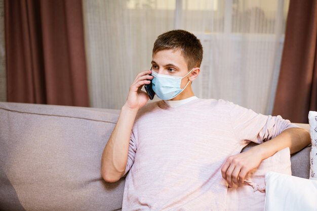 A young man of caucasian appearance in casual clothes talking on the phone in a protective mask whil.