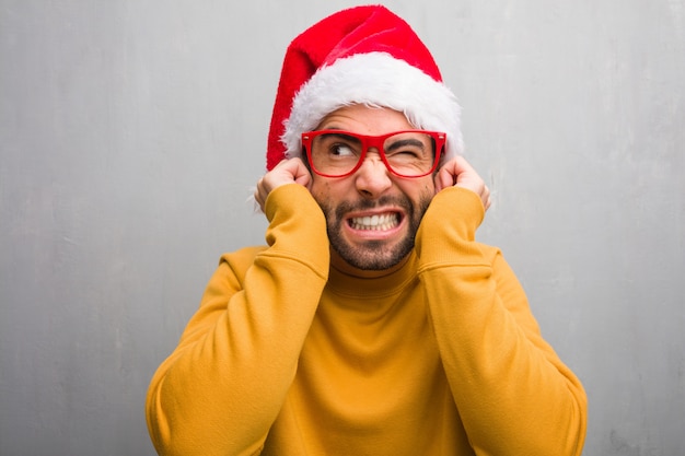 Young man celebrating christmas day holding gifts covering ears with hands