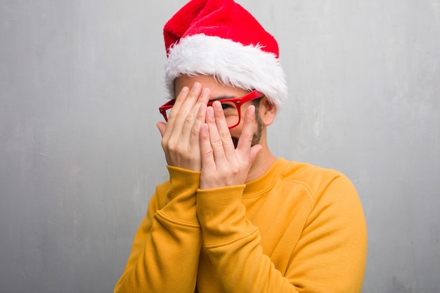 Young man celebrating christmas day holding gifts embarrassed and laughing at the same time