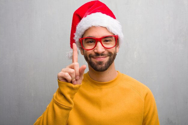 Young man celebrating christmas day holding gifts showing number one
