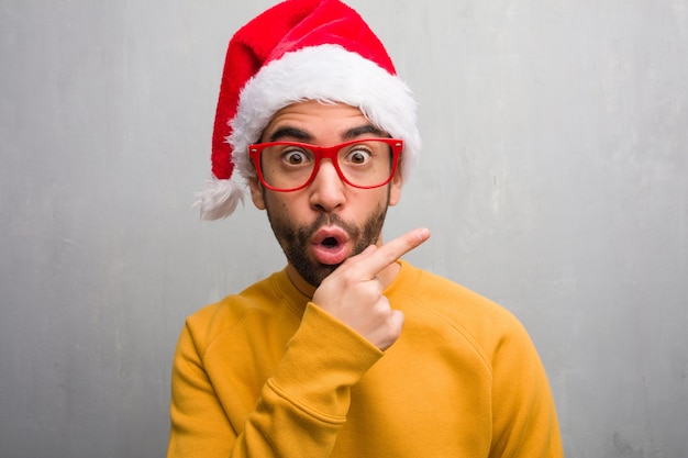 Young man celebrating christmas day holding gifts smiling and pointing to the side