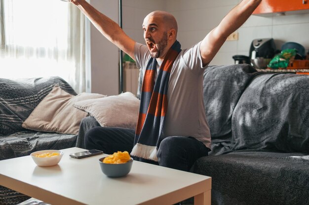 Photo young man celebrating while watching sports on the sofa