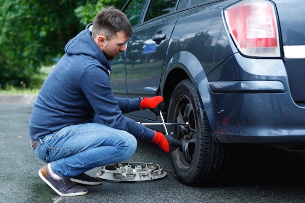 Young man changing flat tire on his car after road accident