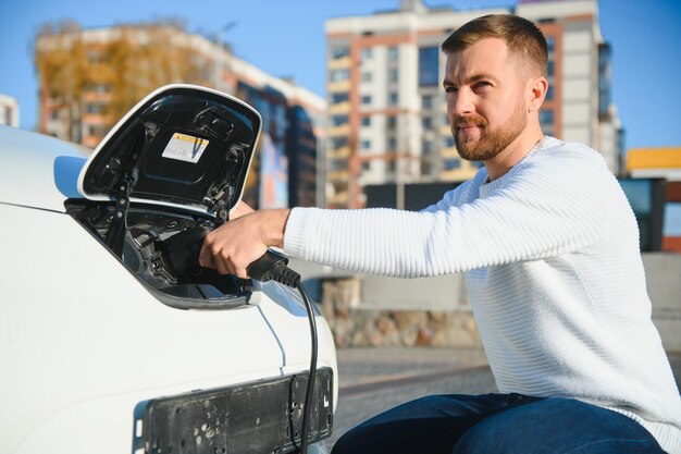 彼の車を充電する若い男