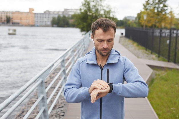 Giovane che controlla il suo polso sul braccialetto fitness durante il suo jogging nel parco