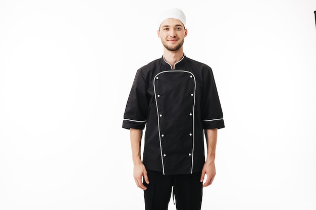 Young man chef in black uniform and white cap dreamily 