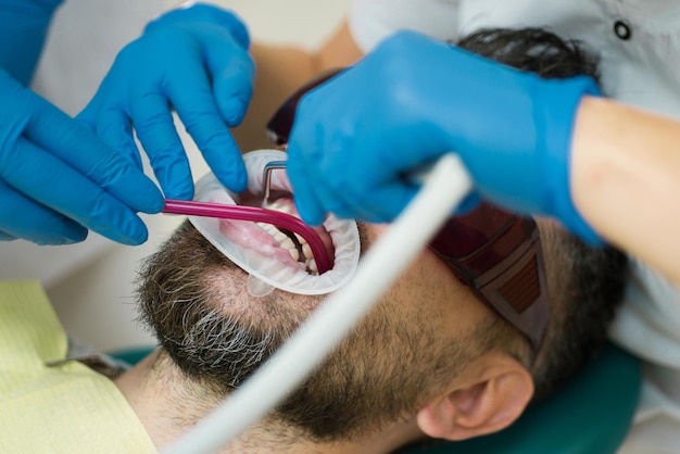 Foto giovane che sceglie il colore dei denti al dentista primo piano dentista femminile che controlla i denti del paziente con mirr