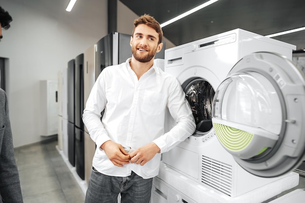 Young man choosing new washing machine in household appliances store