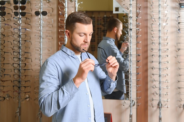 Young man choosing spectacles at optic shop