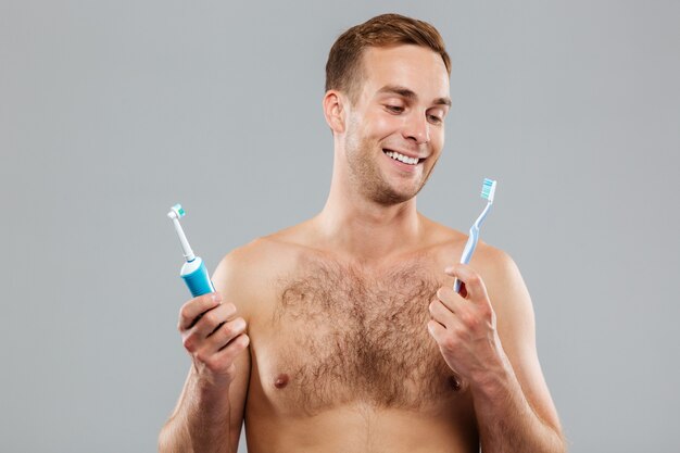 Young man choosing toothbrush isolated on the gray wall