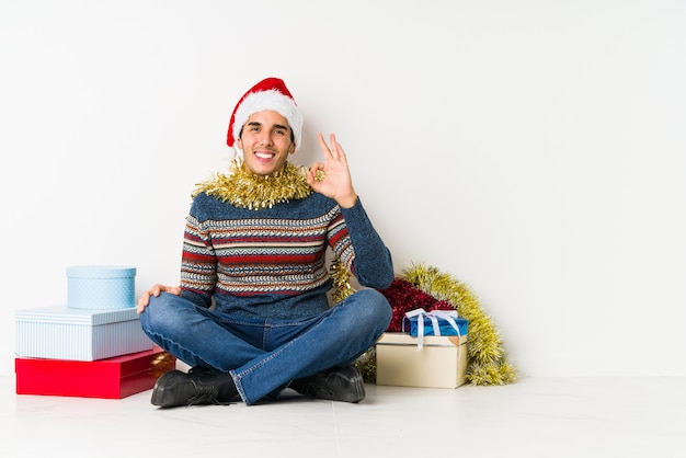 Young man on christmas day makes scale with arms, feels happy and confident.