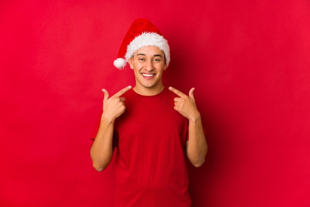 Young man on christmas day smiles, pointing fingers at mouth.