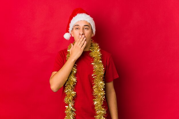 Giovane il giorno di natale che sbadiglia mostrando un gesto stanco che copre la bocca con la mano.