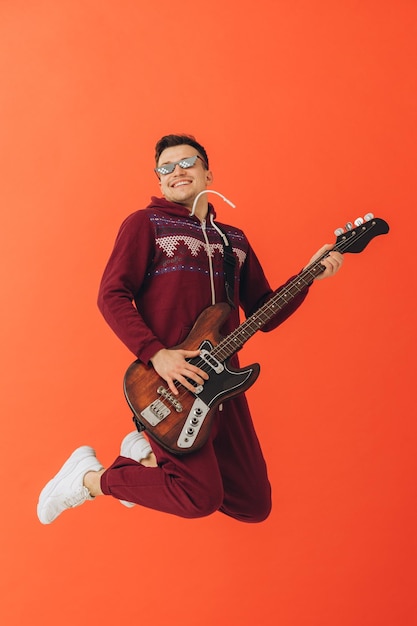 A young man in a Christmas kigurumi plays an electric guitar on a colored background