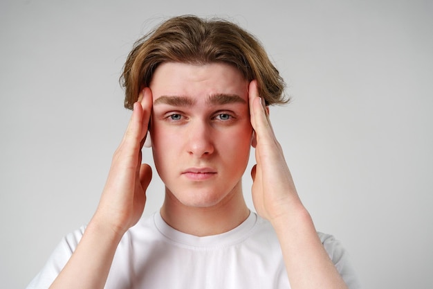 Young man clasping his head seemingly in discomfort or stress against a neutral background