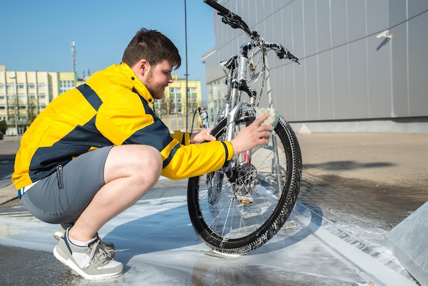 若い男は洗車セルフサービスのライフスタイルで石鹸とスポンジで自転車をきれいにします