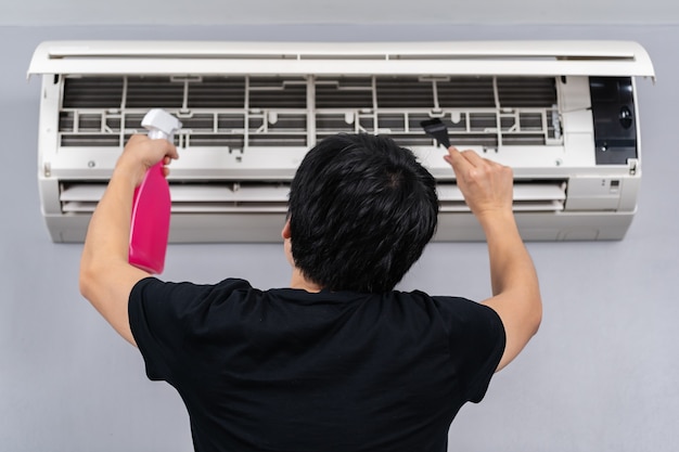 Young man cleaning the air conditioner indoors at home