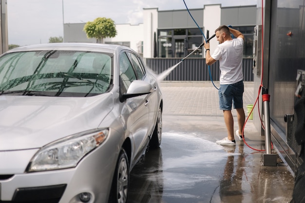 Young man cleaning his car with a jet sprayer selfservice car washing