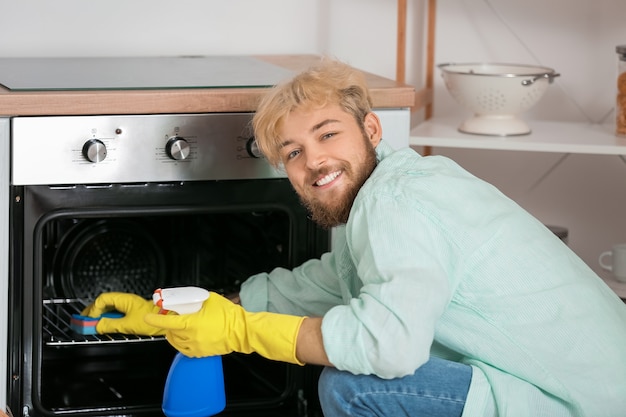 Young man cleaning oven in kitchen