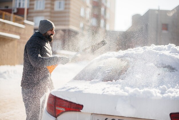 晴れた凍るような日に降雪した後、若い男が車を掃除します。