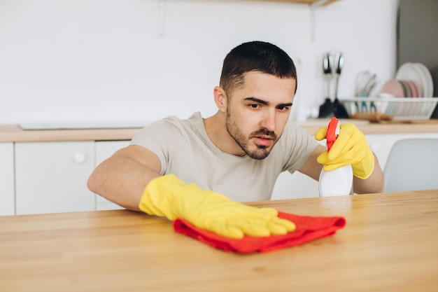 A young man cleans the kitchen at home wipes the table