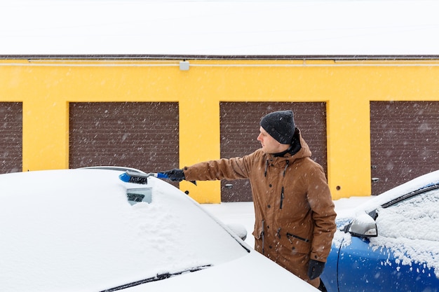 若い男が車から雪をきれいにします。冬のカーケア