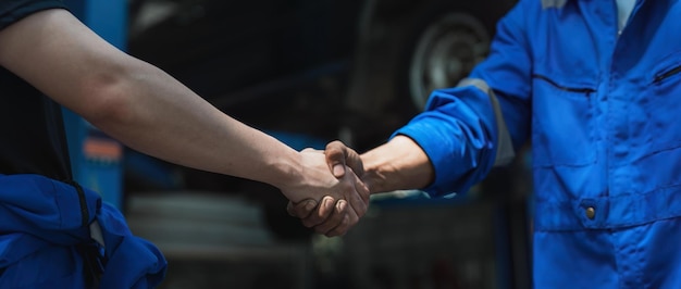 Photo young man client shaking hands with auto mechanic in red uniform having a deal at the car service