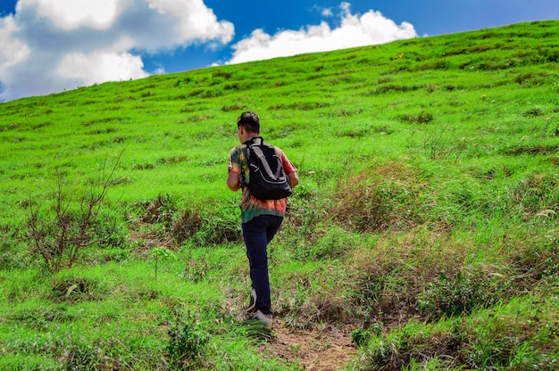 Young man climbing a hill with blue sky back traveler climbing a hill back guy hiking