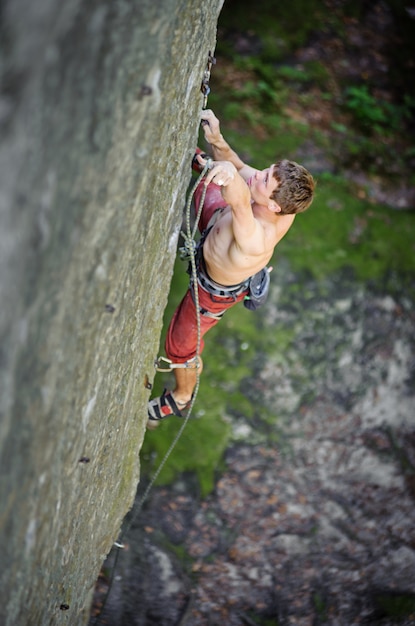 Young man climbing on rock cliff securing carbines and rope