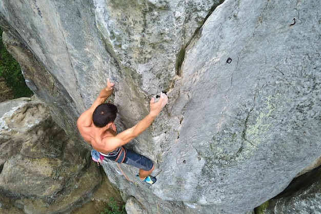 Young man climbing steep wall of rocky mountain. Male climber overcomes challenging route. Engaging in extreme sport concept.