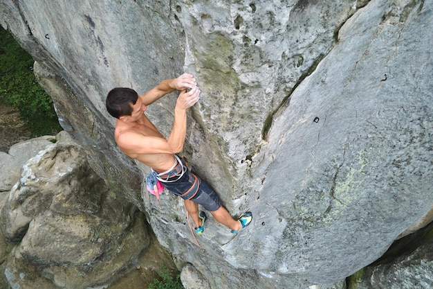 Young man climbing steep wall of rocky mountain Male climber overcomes challenging route Engaging in extreme sport concept