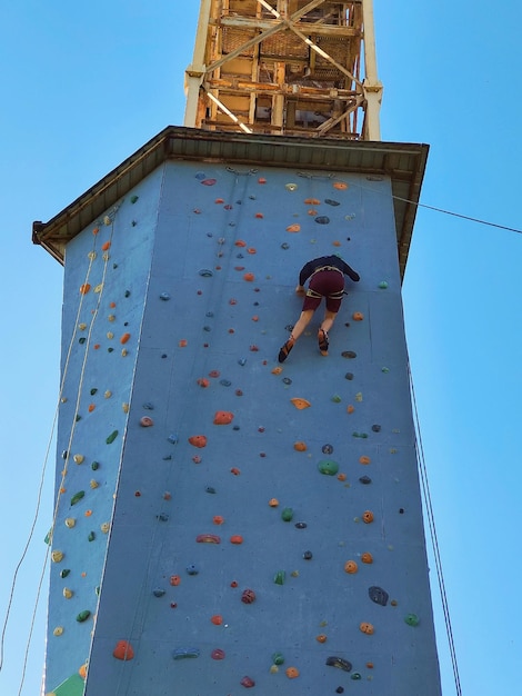 A young man climbs the wall for climbing in special equipment View from below