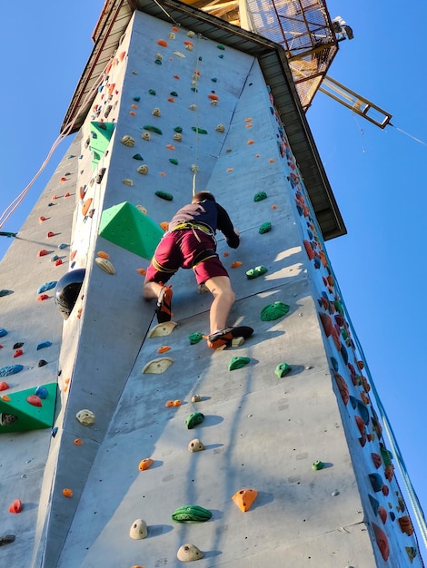 A young man climbs the wall for climbing in special equipment View from below