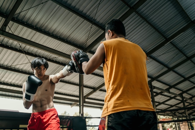 Young man and coach training together with punching pads on the boxing ring at training camp