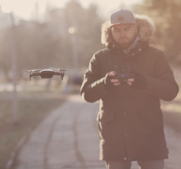 Young man in coat navigating a flying drone in park.