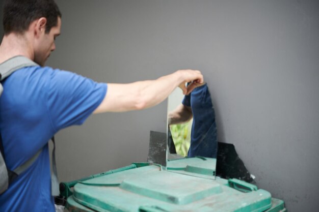 壊れた鏡をリサイクルするためにまたはガラスから芸術作品を作るために集める若い男