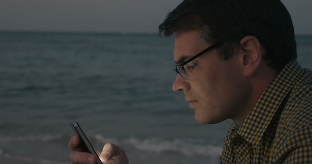 Young man communicating on cell by the sea