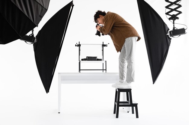 Young man content manager standing on ladder and taking high angle photos of bags working in