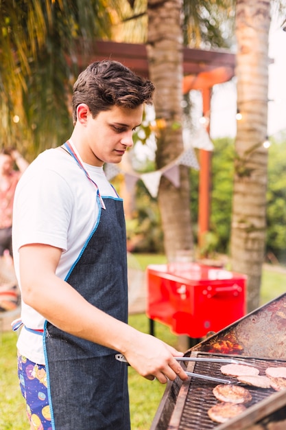 Young man cooking hamburgers on the outdoor grill in the sun