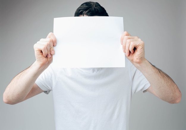 Young man covering his face with white blank paper sheet