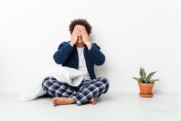 Young man covers eyes with hands, smiles broadly waiting for a surprise