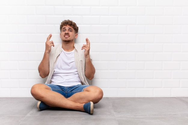 Young man crossing fingers anxiously and hoping for good luck with a worried look