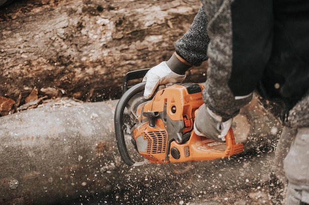 Photo young man cutting the huge felled wood by chainsaw create winter wood stocks industrial concept