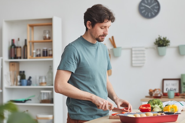 Фото Молодой человек режет овощи для блюда, стоя на домашней кухне