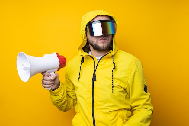 Young man in cyberpunk glasses holding a megaphone on a yellow background