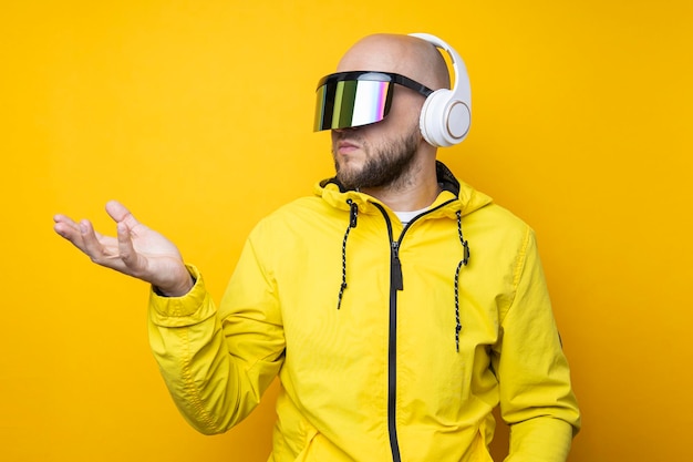 Young man in cyberpunk glasses with headphones holding an invisible object on a yellow background