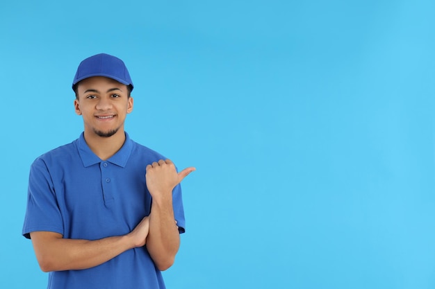 Young man in delivery uniform on blue background