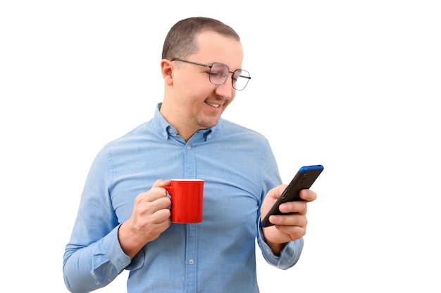 Young man in denim shirt having hot drink using mobile phone on white background