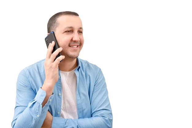 Молодой человек в джинсовой рубашке разговаривает по мобильному телефону на белом фоне