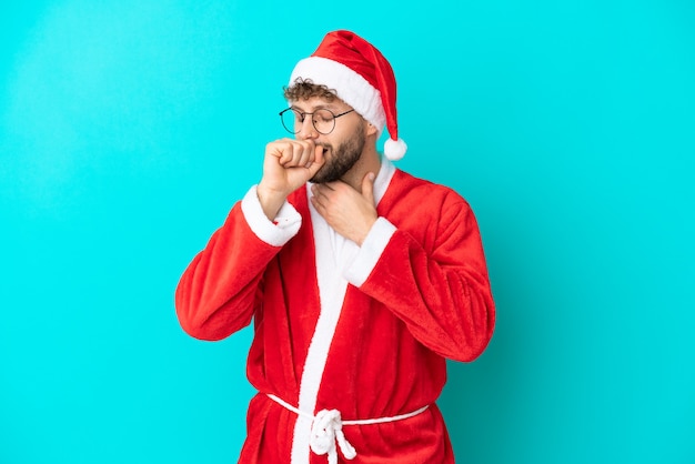 Young man disguised as Santa Claus isolated on blue background is suffering with cough and feeling bad